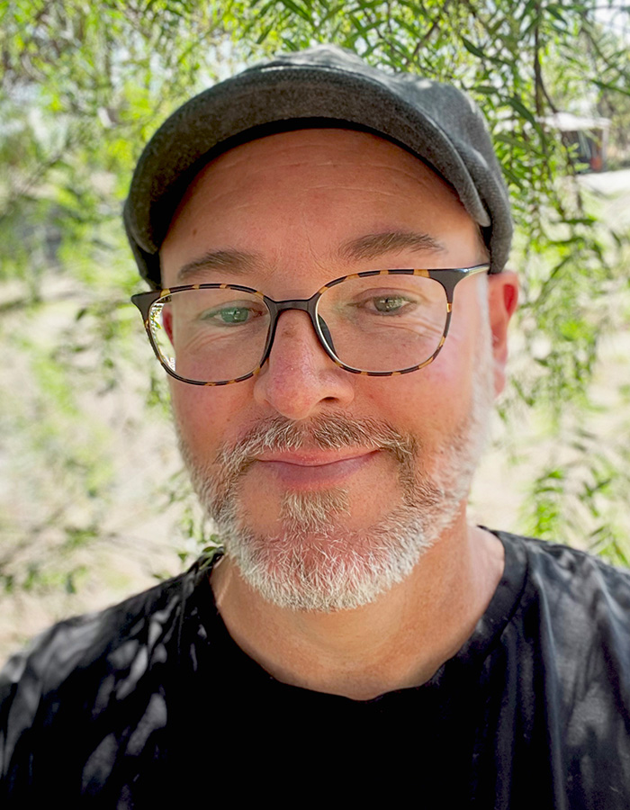 A photo of Brock in a flat cap in front of a pepper tree
